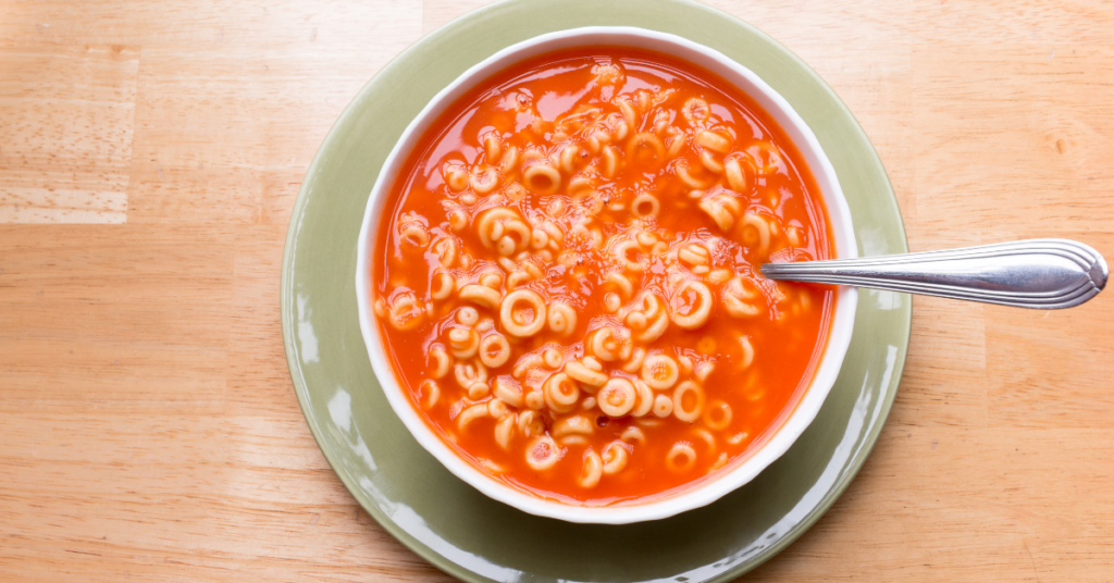 A bowl of pasta soup with a spoon.